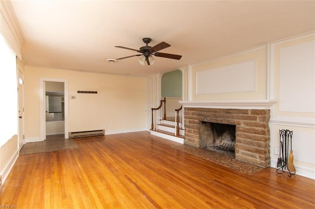 unfurnished living room featuring a ceiling fan, wood finished floors, stairway, a fireplace, and a baseboard radiator