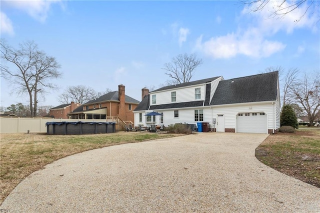 back of house with fence, a covered pool, a shingled roof, a garage, and aphalt driveway