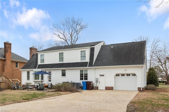 back of property with a garage, roof with shingles, driveway, and a patio area