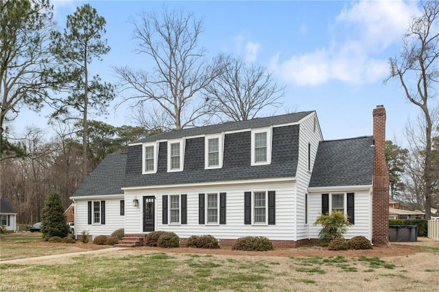 dutch colonial featuring a chimney, a shingled roof, and a front yard