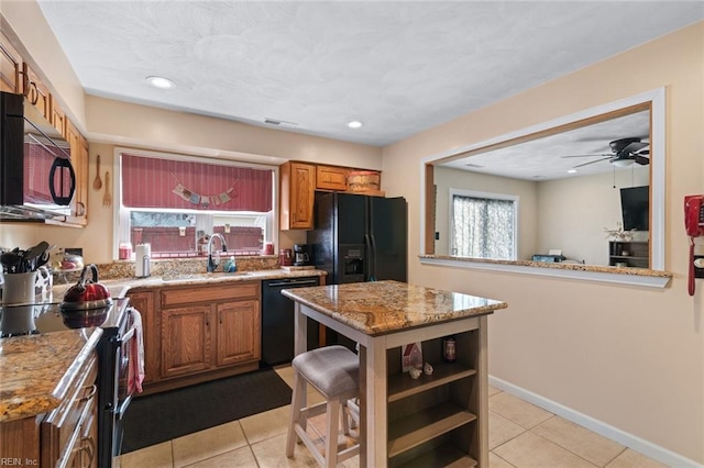 kitchen with light stone counters, light tile patterned floors, brown cabinets, black appliances, and a sink