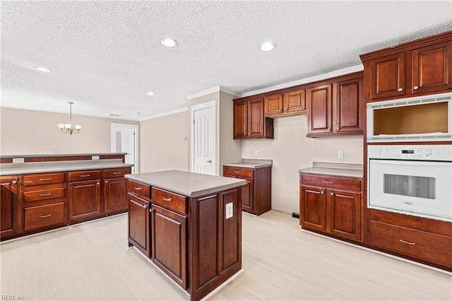 kitchen with pendant lighting, light wood-style flooring, a center island, white oven, and a chandelier