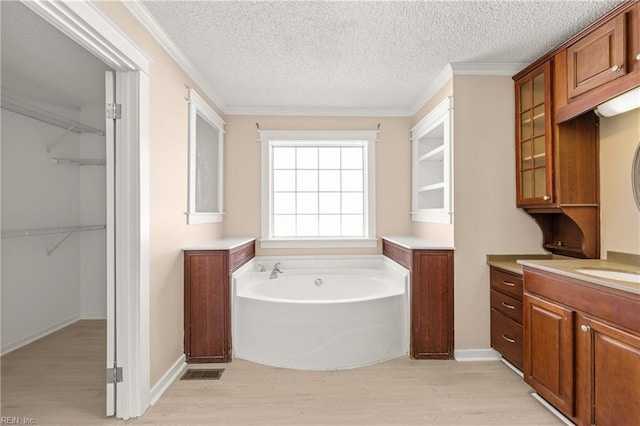 bathroom featuring a walk in closet, a garden tub, a textured ceiling, wood finished floors, and vanity