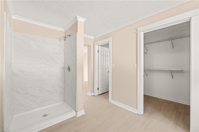 bathroom with ornamental molding, a textured ceiling, wood finished floors, a shower stall, and baseboards