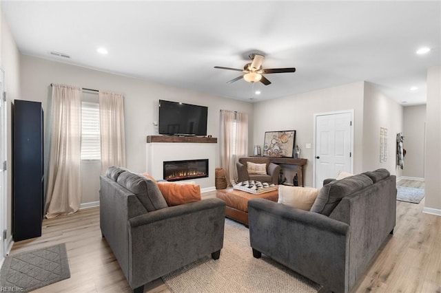 living room featuring a glass covered fireplace, light wood-style flooring, recessed lighting, and a ceiling fan