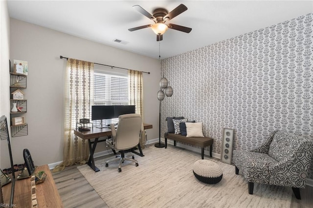 office area featuring visible vents, wallpapered walls, baseboards, wood finished floors, and a ceiling fan