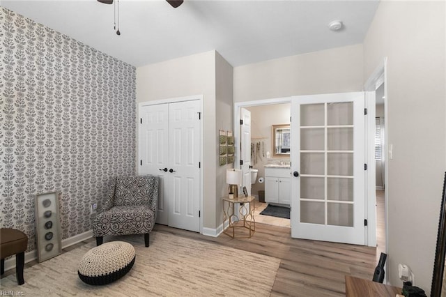 sitting room with ceiling fan, baseboards, wood finished floors, and wallpapered walls