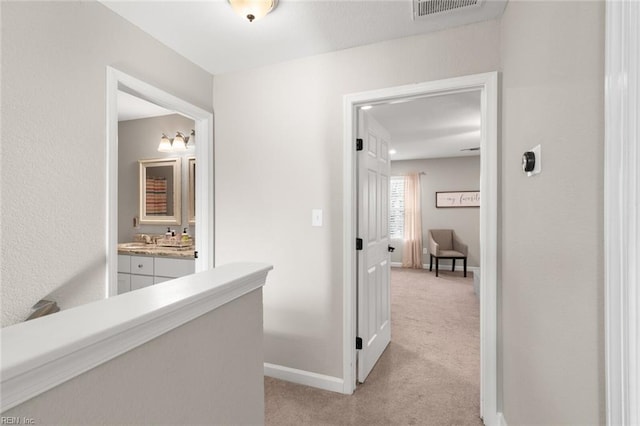 hallway featuring light carpet, visible vents, baseboards, and a sink