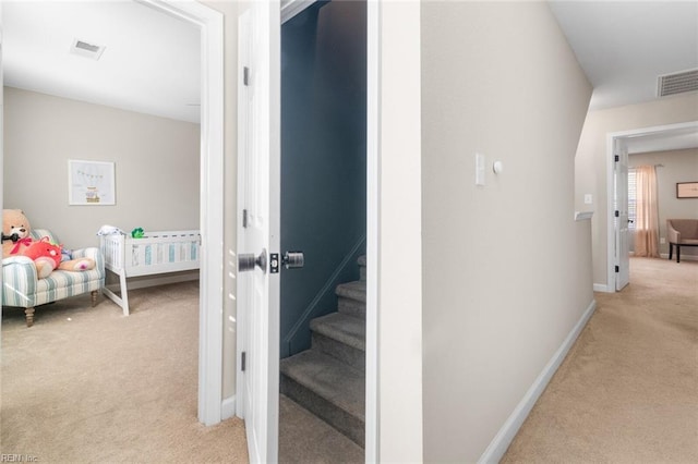 hallway with visible vents, baseboards, light colored carpet, and stairway