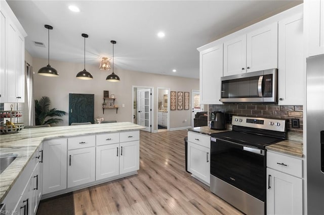 kitchen featuring visible vents, a peninsula, light wood-style flooring, stainless steel appliances, and backsplash