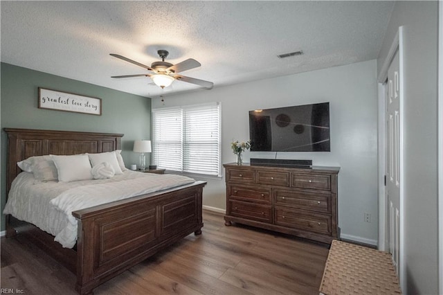 bedroom featuring visible vents, a textured ceiling, wood finished floors, baseboards, and ceiling fan