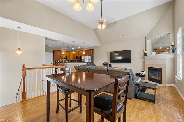 dining room with visible vents, light wood-style flooring, a tile fireplace, and vaulted ceiling