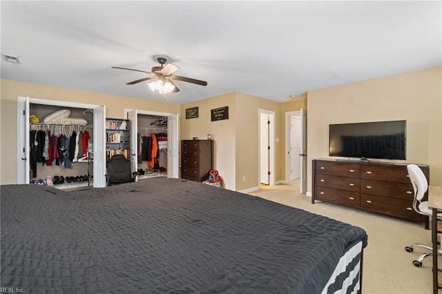 bedroom with a ceiling fan, visible vents, baseboards, light colored carpet, and two closets