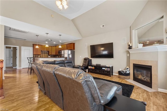 living area featuring visible vents, a tile fireplace, light wood-style floors, and vaulted ceiling