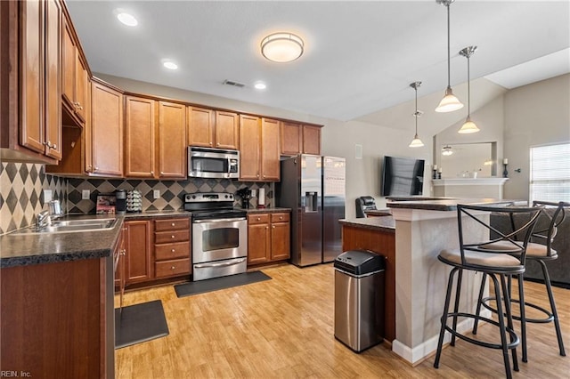 kitchen featuring visible vents, a breakfast bar, light wood-style flooring, appliances with stainless steel finishes, and dark countertops