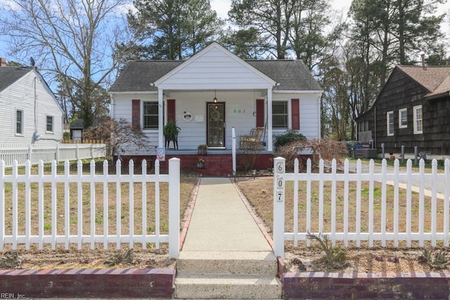 bungalow with a fenced front yard, covered porch, a front lawn, and a shingled roof