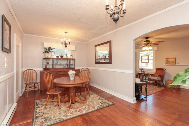 dining area featuring wood finished floors, a wainscoted wall, a baseboard radiator, arched walkways, and a textured ceiling