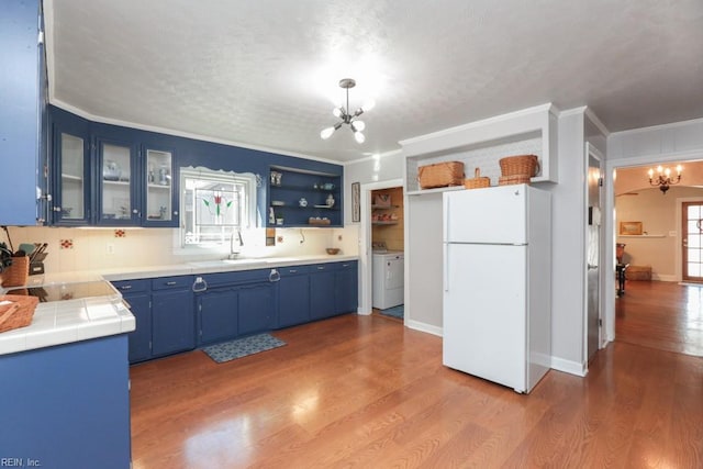 kitchen featuring wood finished floors, blue cabinetry, freestanding refrigerator, a sink, and a notable chandelier