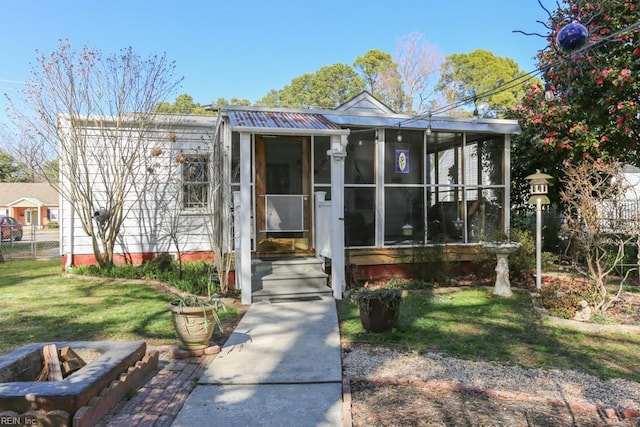 bungalow featuring a front lawn, fence, an outdoor fire pit, metal roof, and a sunroom