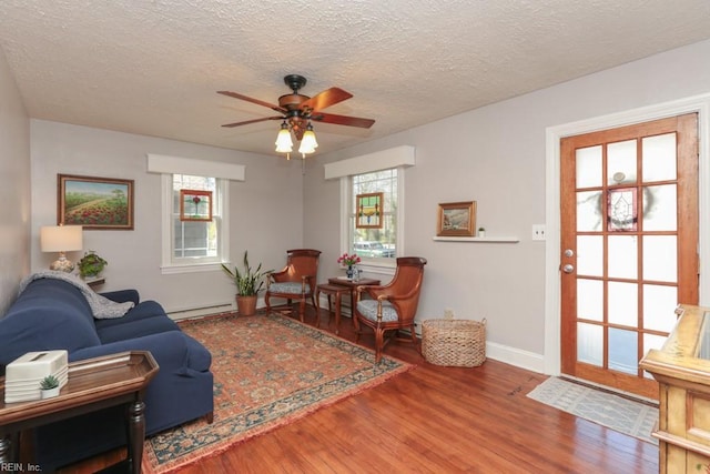 living room featuring baseboard heating, a healthy amount of sunlight, a ceiling fan, and wood finished floors