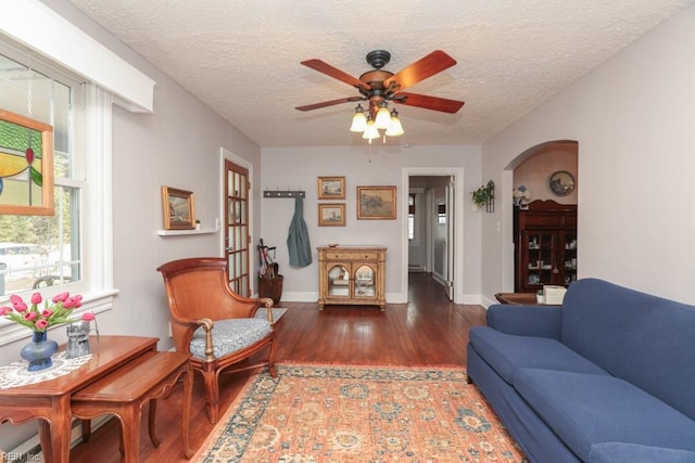 living area featuring a ceiling fan, a textured ceiling, wood finished floors, arched walkways, and baseboards