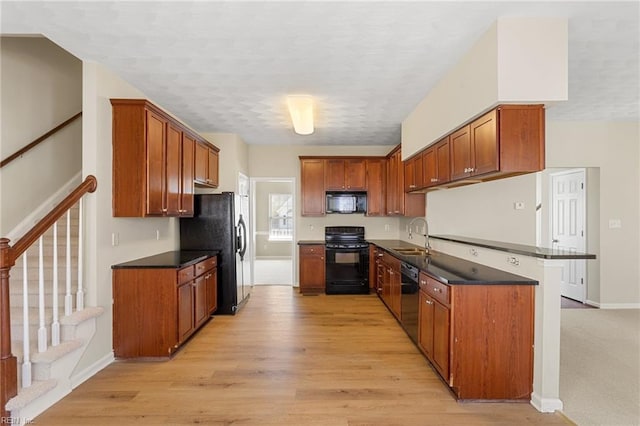 kitchen featuring brown cabinetry, light wood finished floors, a sink, black appliances, and dark countertops