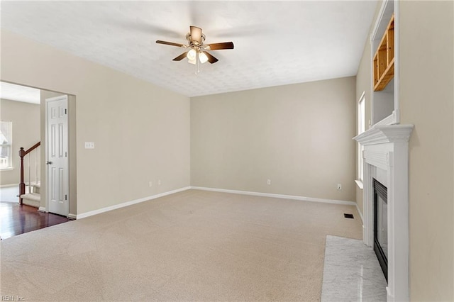 unfurnished living room with a fireplace with flush hearth, a ceiling fan, stairway, carpet floors, and baseboards