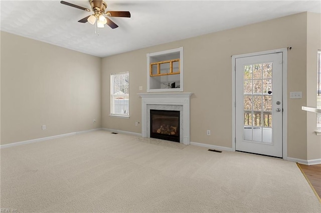 unfurnished living room featuring a high end fireplace, visible vents, baseboards, carpet flooring, and a ceiling fan