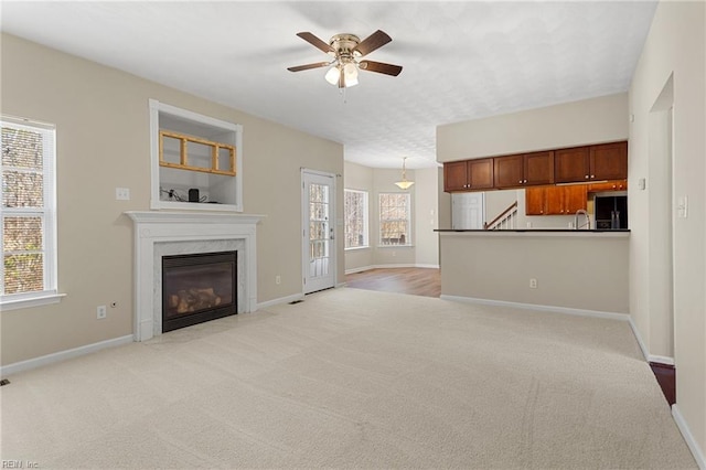 unfurnished living room with a premium fireplace, light carpet, baseboards, and ceiling fan