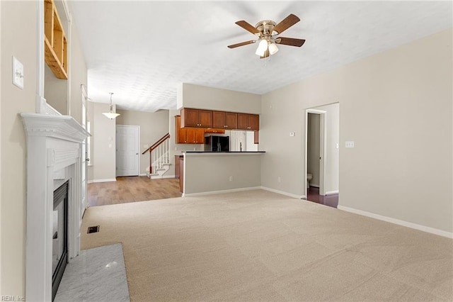 unfurnished living room featuring ceiling fan, baseboards, stairs, light carpet, and a fireplace