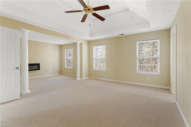 spare room with baseboards, a tray ceiling, decorative columns, light carpet, and a glass covered fireplace