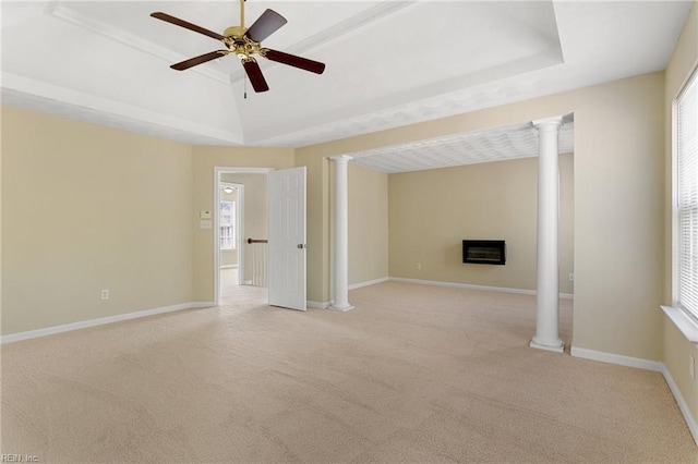 empty room featuring a tray ceiling, baseboards, a glass covered fireplace, and ornate columns