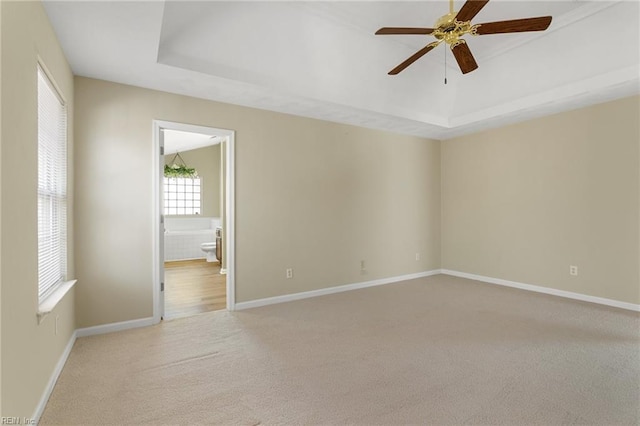 spare room featuring carpet flooring, ceiling fan, a raised ceiling, and baseboards