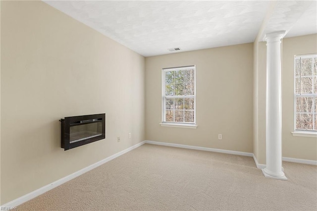 carpeted spare room with decorative columns, plenty of natural light, baseboards, and a glass covered fireplace