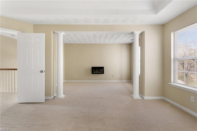 spare room featuring a glass covered fireplace, decorative columns, carpet, and baseboards