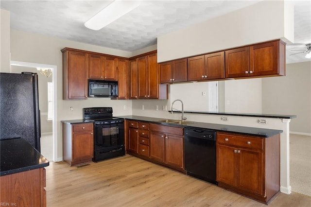 kitchen with light wood finished floors, ceiling fan, a peninsula, black appliances, and a sink