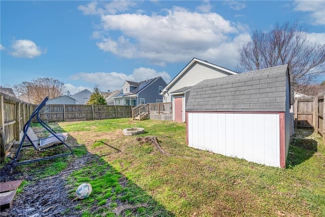 view of yard featuring a shed, an outdoor fire pit, a fenced backyard, a deck, and an outbuilding