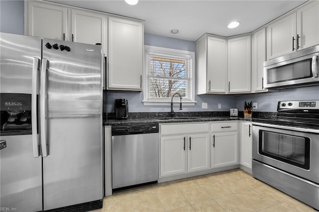 kitchen featuring white cabinetry, stainless steel appliances, dark stone counters, and a sink