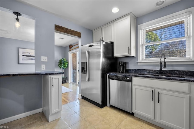 kitchen with dark stone countertops, light tile patterned floors, a sink, stainless steel appliances, and white cabinetry