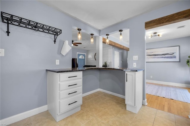 kitchen with dark stone countertops, baseboards, light tile patterned floors, and white cabinetry