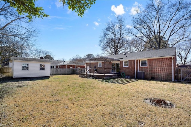 back of property featuring brick siding, a fenced backyard, a yard, crawl space, and a deck