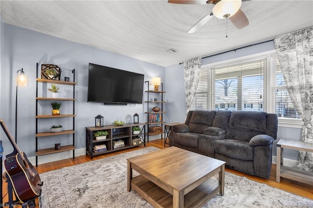 living area featuring baseboards, a textured ceiling, wood finished floors, and a ceiling fan