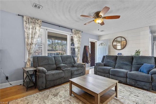 living area featuring visible vents, a ceiling fan, a textured ceiling, wood finished floors, and baseboards