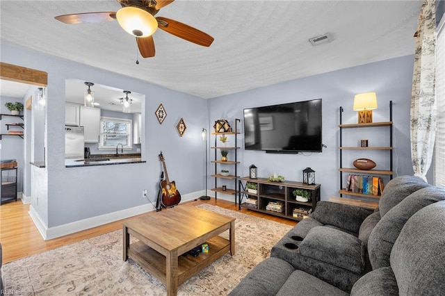 living room with light wood-style flooring, visible vents, baseboards, and ceiling fan