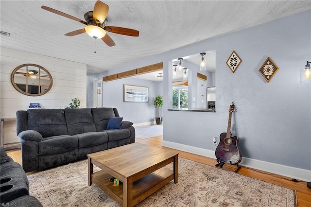 living room with a ceiling fan, baseboards, light wood finished floors, and a textured ceiling