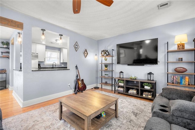 living room with a ceiling fan, light wood-style flooring, visible vents, and baseboards