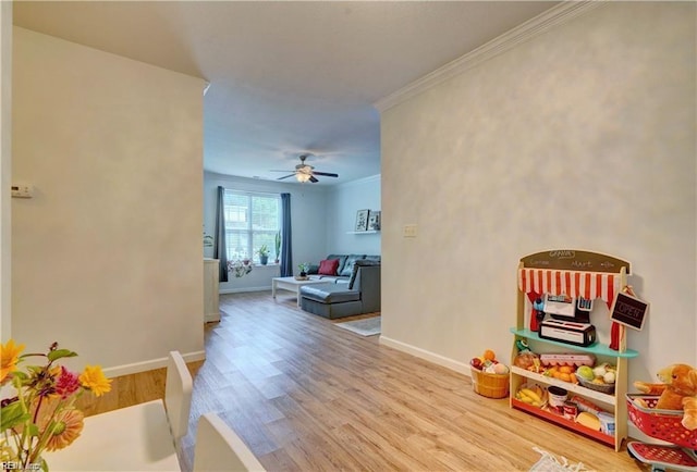 rec room featuring crown molding, light wood-style flooring, baseboards, and ceiling fan