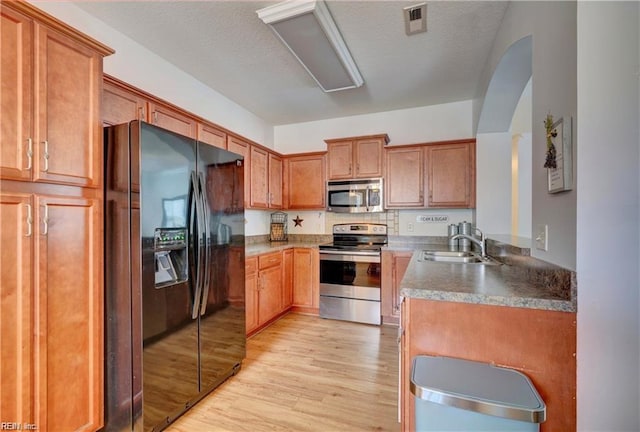 kitchen with brown cabinets, light wood-style floors, arched walkways, stainless steel appliances, and a sink