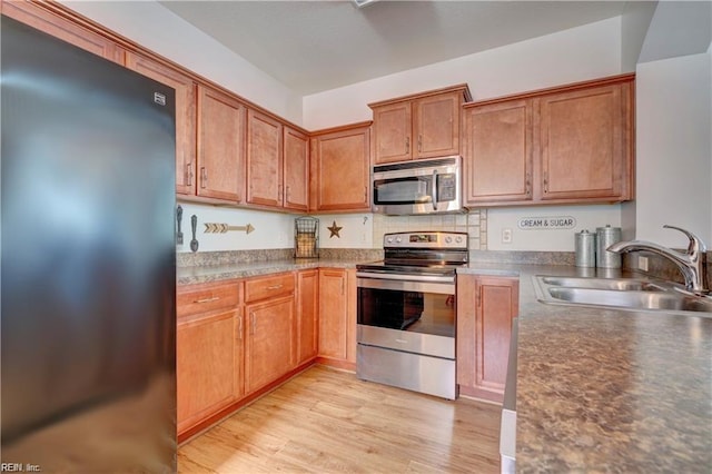 kitchen with a sink, light wood-type flooring, brown cabinets, and appliances with stainless steel finishes