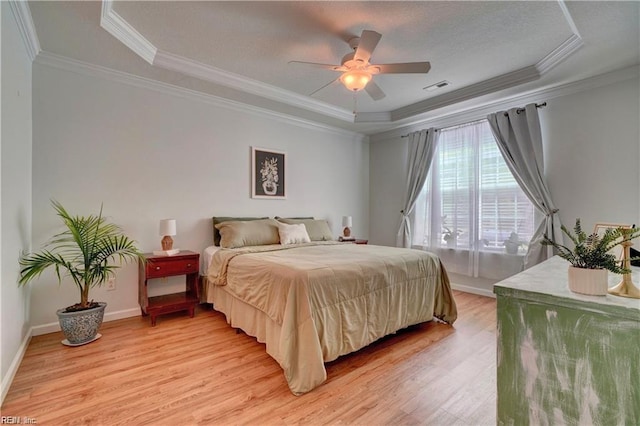 bedroom with light wood-type flooring, a raised ceiling, and crown molding